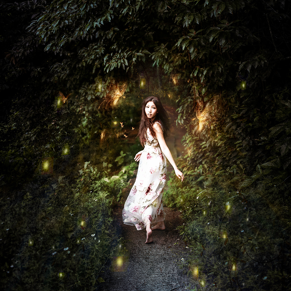 Woman in a white dress in a forest of fireflies - surreal photo by Cathryn Mok
