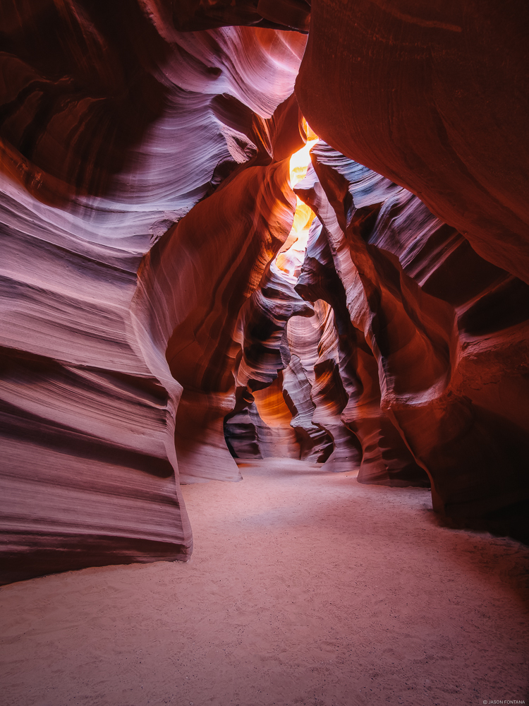 Layered red-orange rock walls around a narrow canyon with bright light above