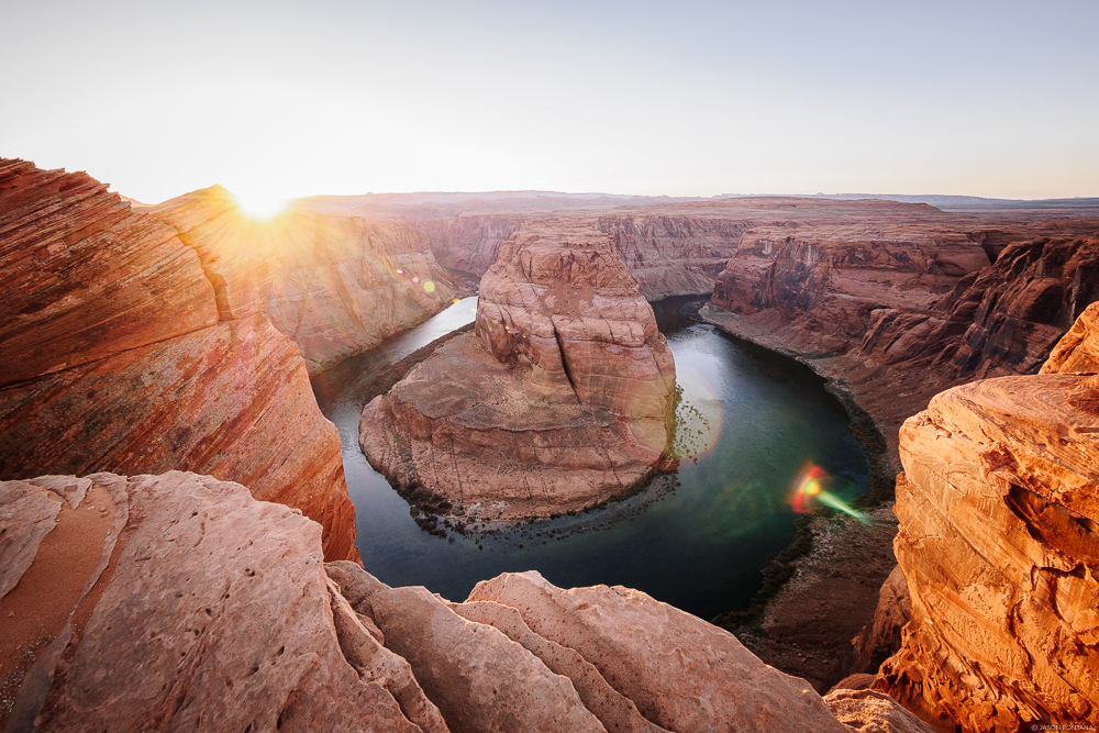 Curving river around a large rock mass with warm sun near the canyon horizon