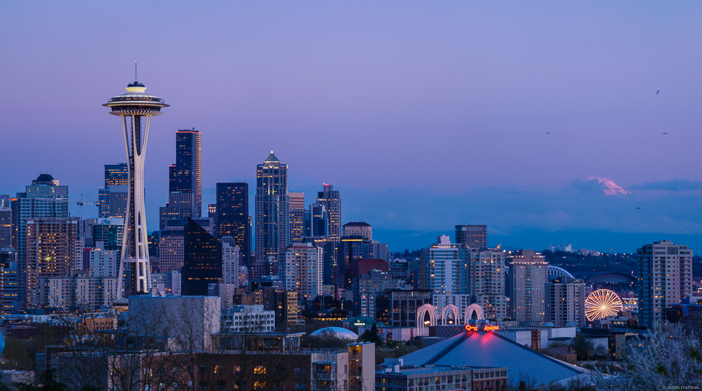 City skyline with a tall observation tower beneath a lavender twilight sky