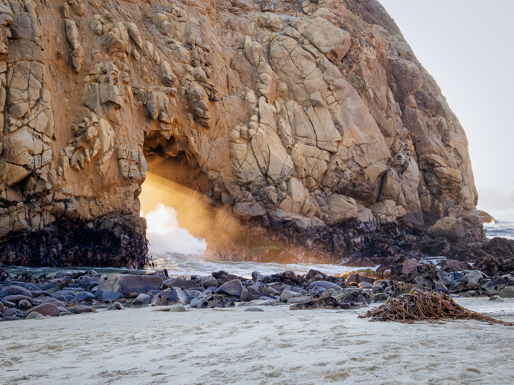 Rock arch above foamy coastal water with warm light visible through the opening