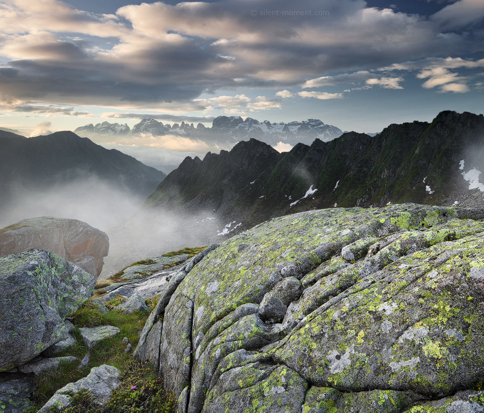 Lichen-covered foreground rocks above mist and distant mountain ridges in Val Nambrone toward the Brenta massif, Trentino, Italy