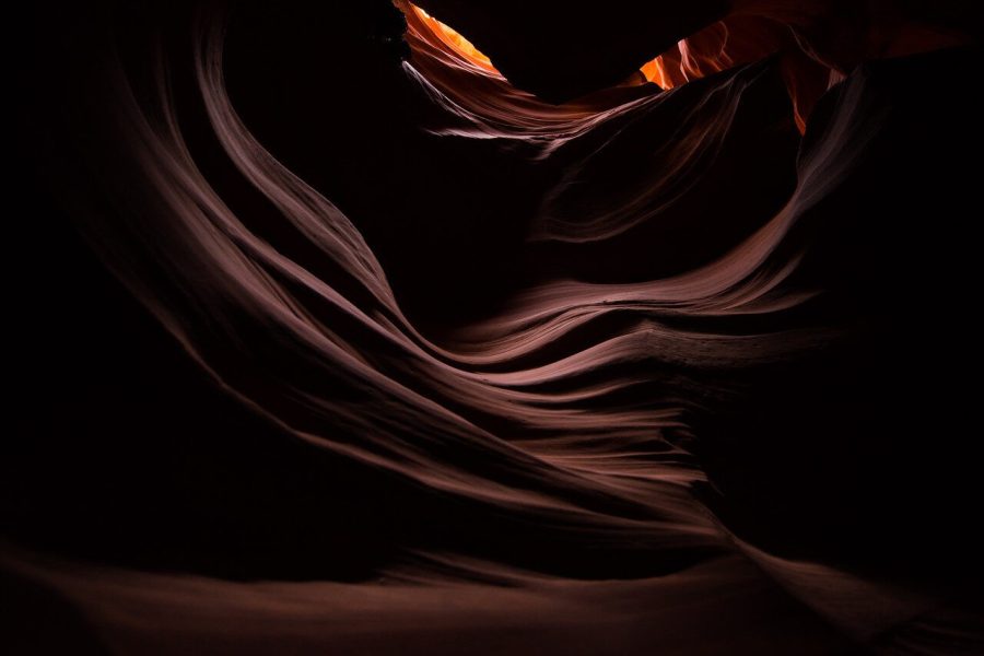 Layered sandstone curves around a narrow warm opening in a slot canyon
