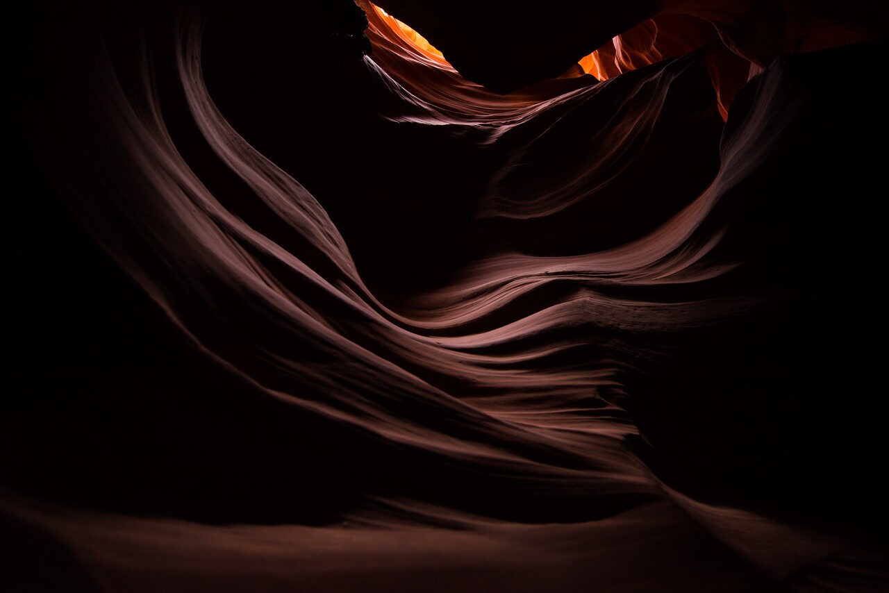 Layered sandstone curves around a narrow warm opening in a slot canyon