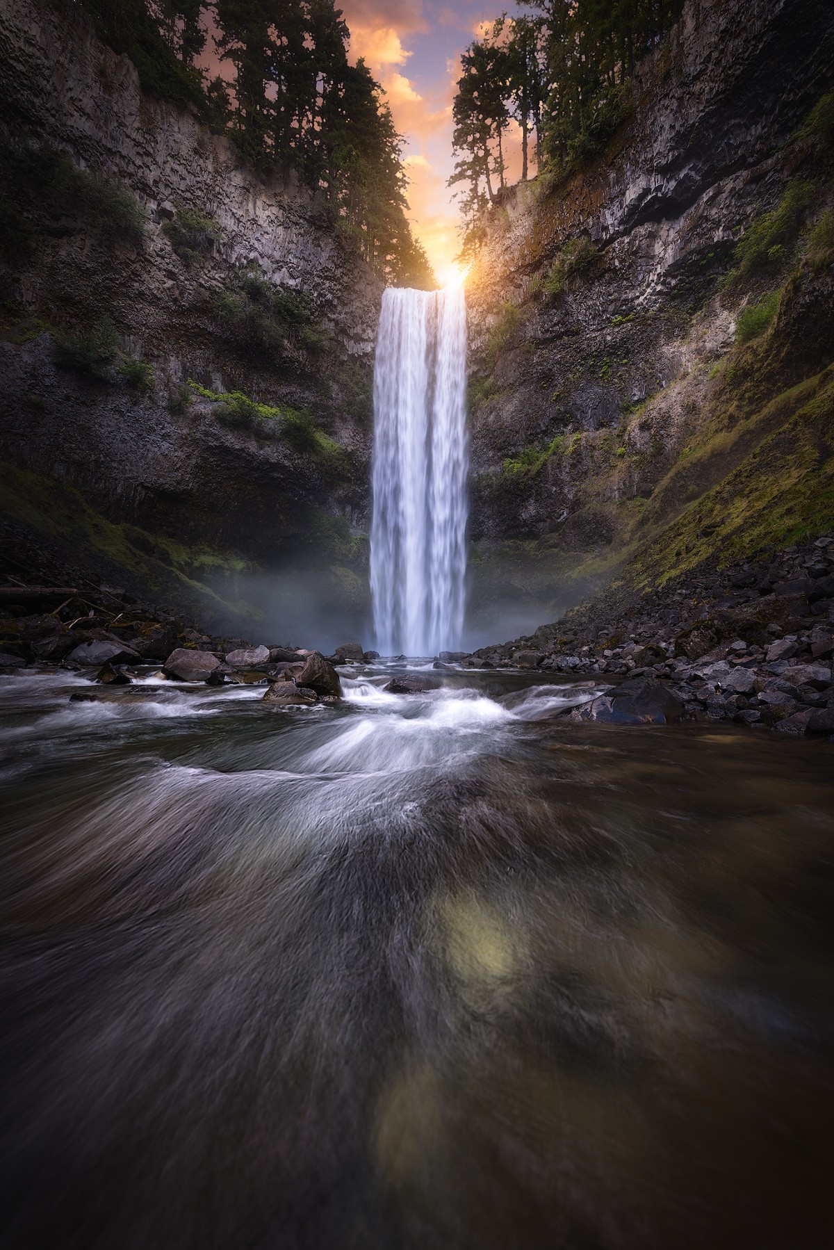 Tall waterfall between dark canyon walls with flowing water in the foreground
