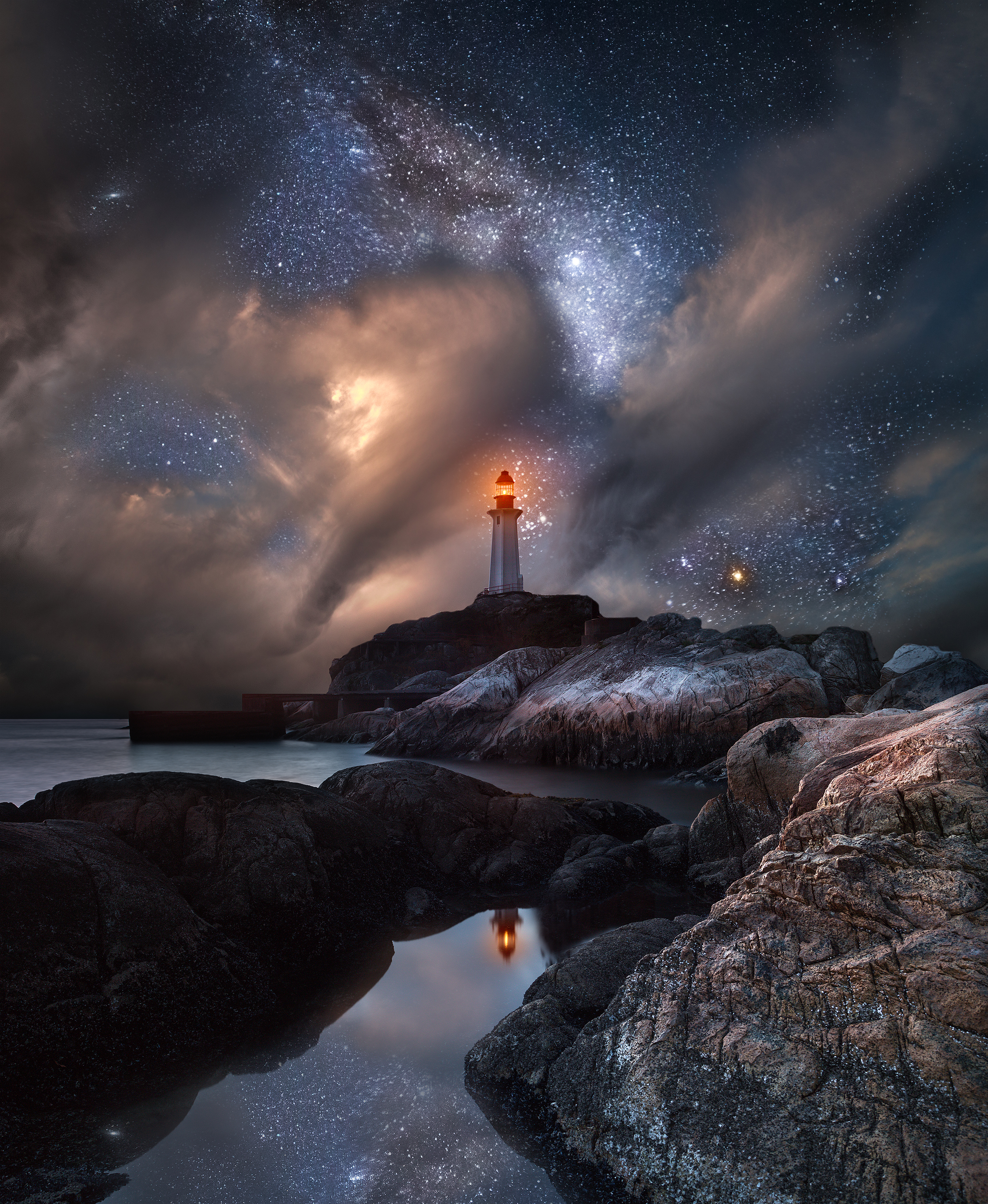 Lighthouse with a warm beacon above coastal rocks and a reflective pool under stars and clouds