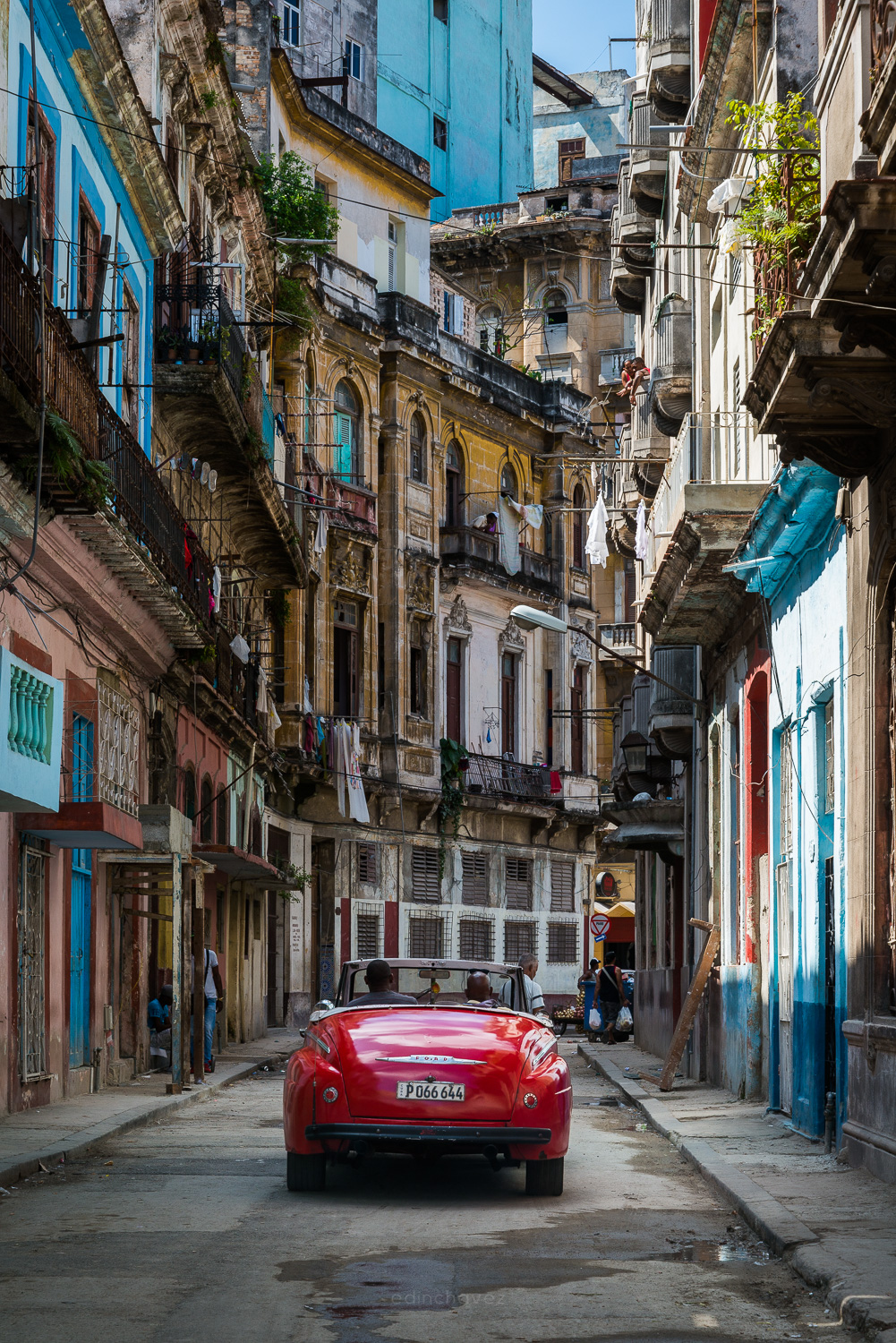 Red convertible on a narrow street beneath balconies and tall buildings