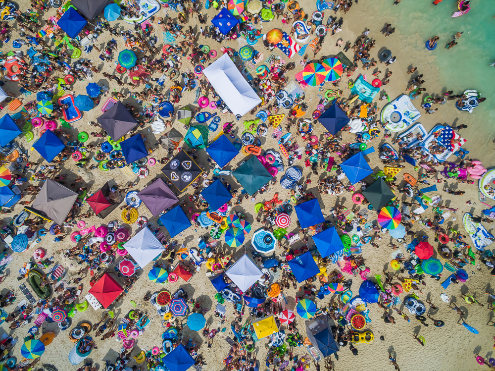 Top-down view of a crowded beach covered with colorful tents, umbrellas, towels and inflatables