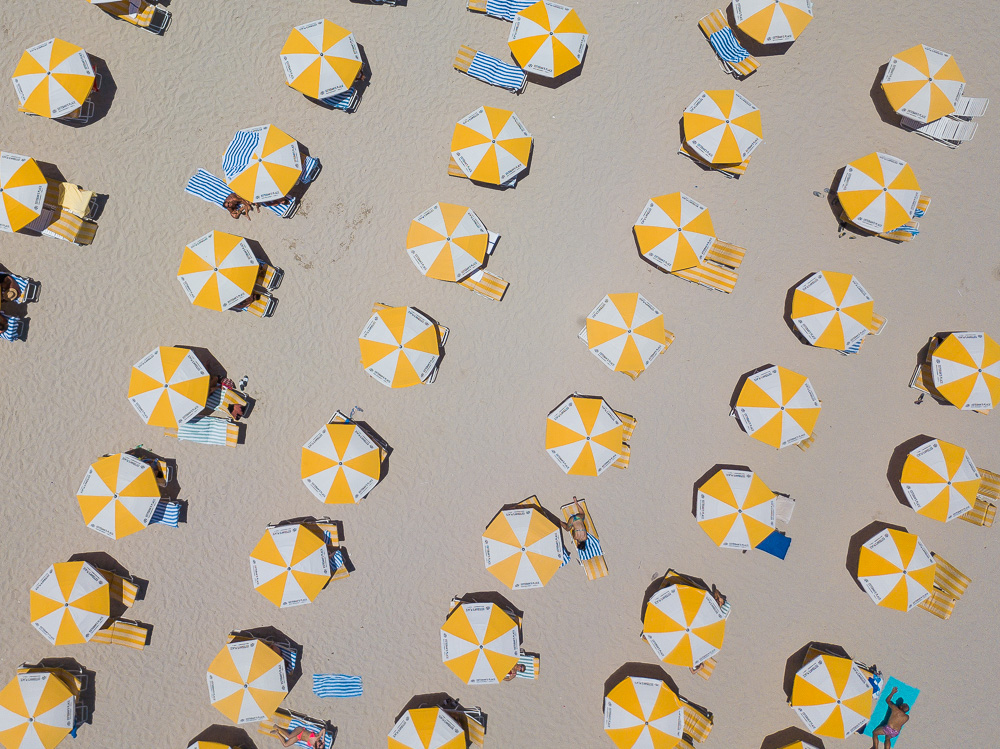 Aerial view of yellow and white umbrellas and striped lounge chairs on a sandy beach