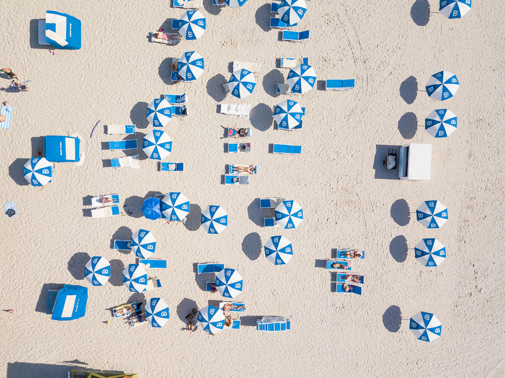 Aerial view of blue and white umbrellas, lounge chairs, and sunbathers on a sandy beach