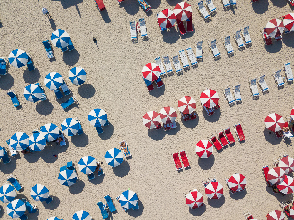 Aerial view of red and blue umbrellas and rows of lounge chairs on a crowded sandy beach
