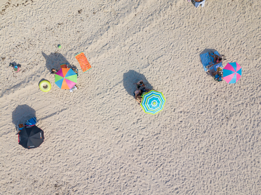 Aerial view of beachgoers relaxing under colorful umbrellas on a sandy beach