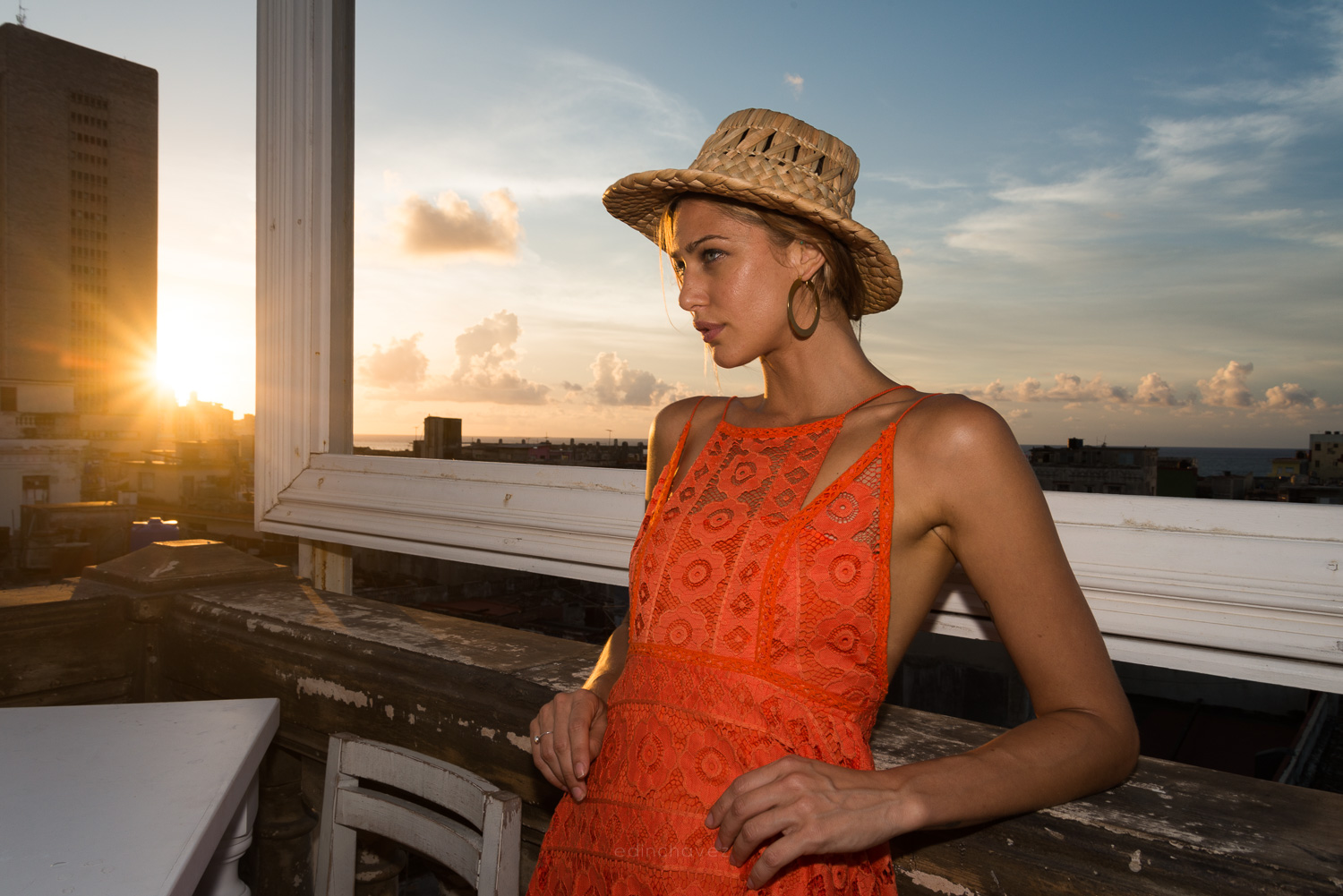 Woman wearing a straw hat beside a rooftop window at sunset