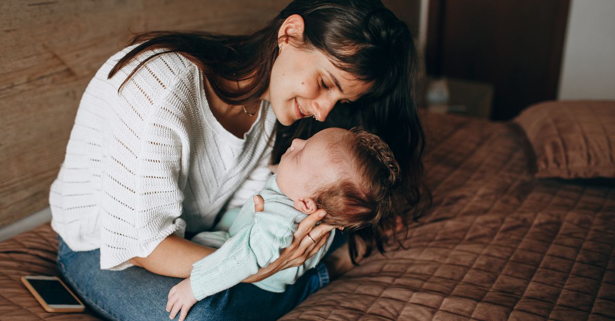 Seated mother looking down at her baby held in her arms indoors