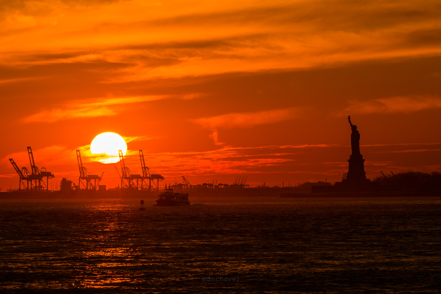 Statue of Liberty silhouette separated from an orange sunset sky over the water