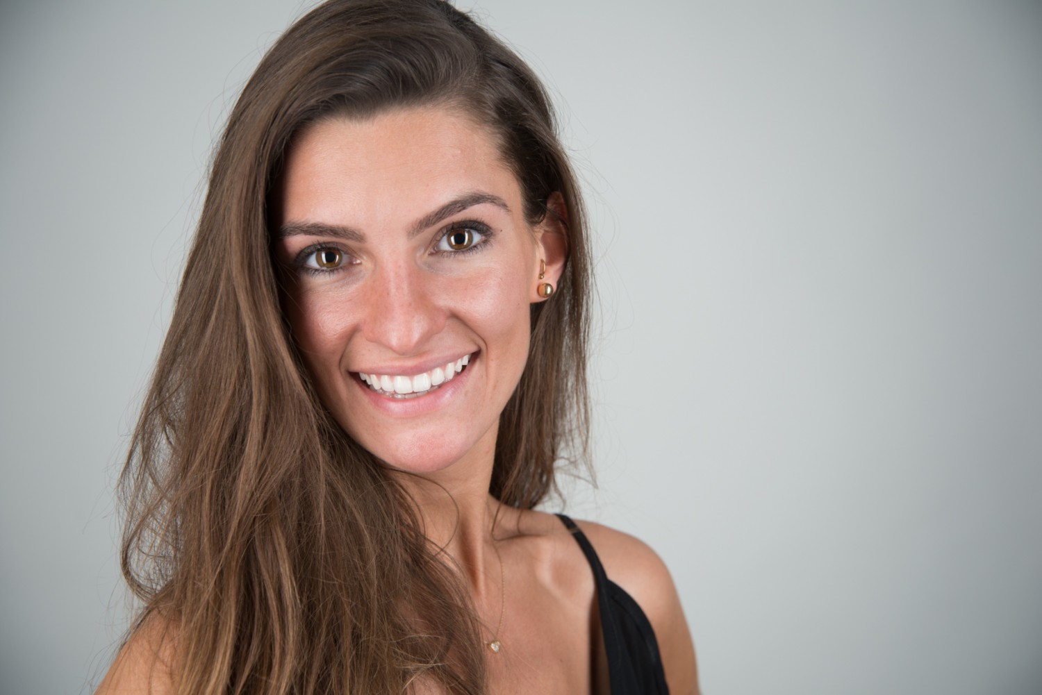 Smiling woman with long brown hair in a close-up headshot against a gray background.