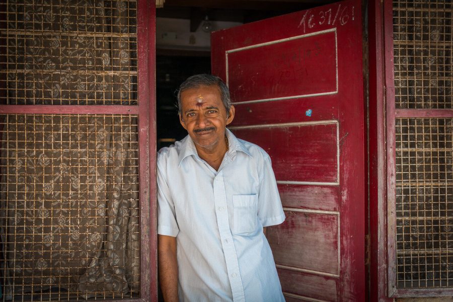 Portrait of a man in a white shirt beside a red doorway in India