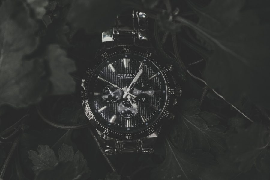 Black chronograph wristwatch with silver hands and markers among dark leaves