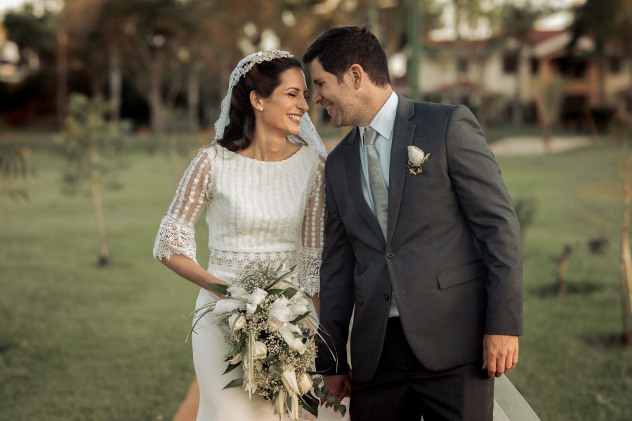 A wedding couple smiling together outdoors with a bouquet