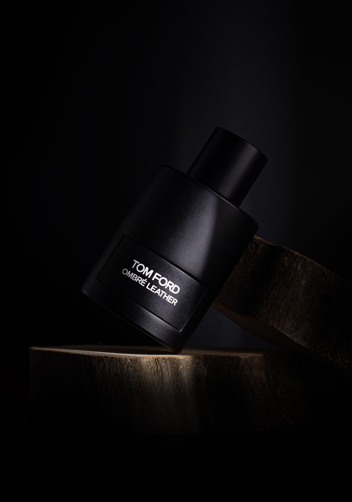 Black perfume bottle with a readable white label resting at an angle on dark wood