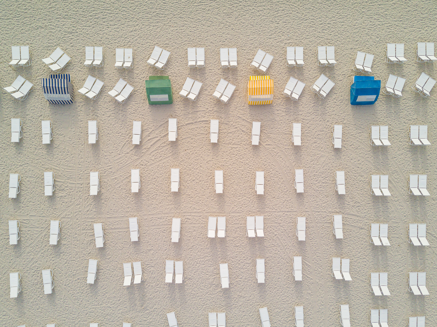 Overhead view of rows of white beach chairs and colored beach tents on sand