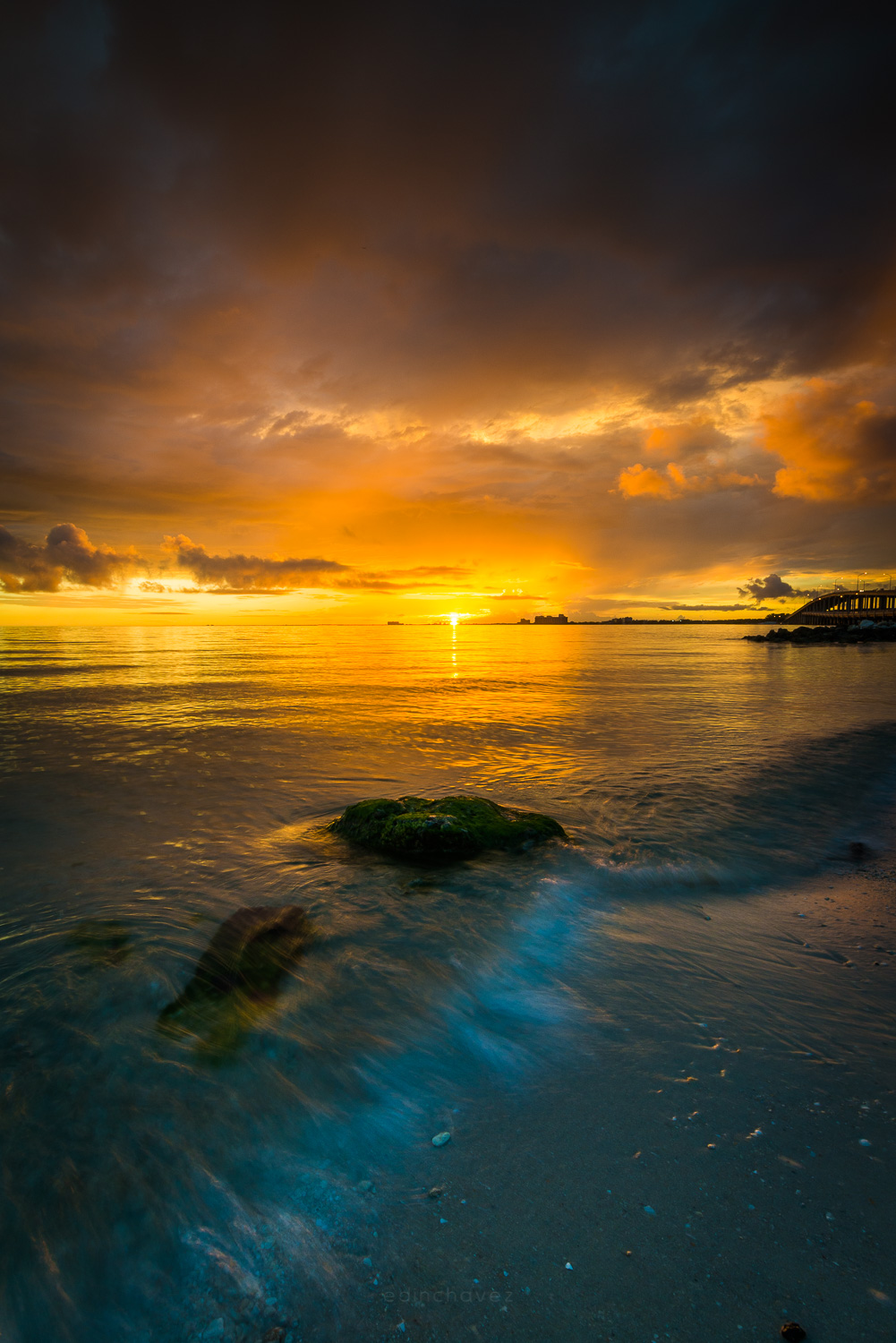 Golden sunset over the water with a mossy rock and smoothed wave motion in the foreground