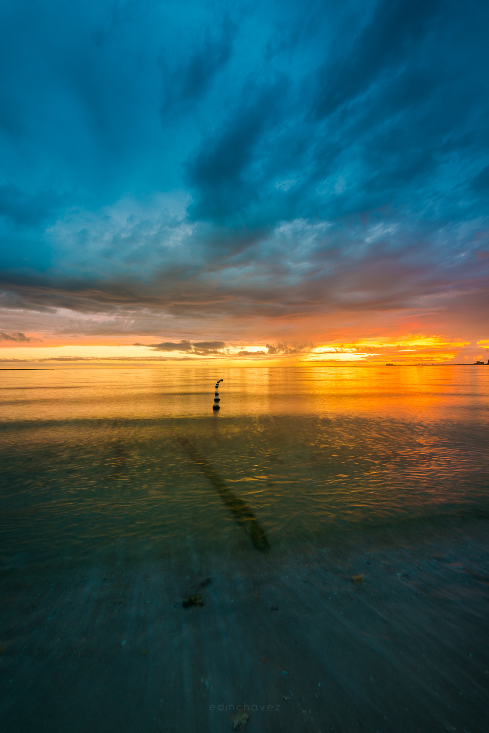 Teal and blue dusk sky with dark clouds over shallow water on a beach, with soft motion in the foreground