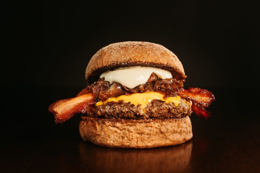 Bacon cheeseburger with melted cheese and caramelized onions against a black background