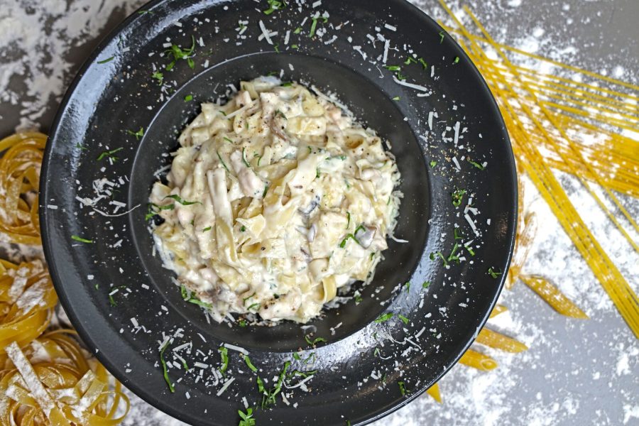 Overhead view of creamy pasta on a black plate surrounded by uncooked noodles and grated cheese