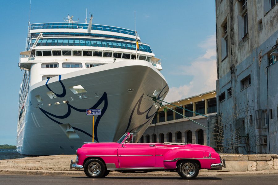 Bright pink vintage convertible beside a docked cruise ship and weathered waterfront buildings in Havana, Cuba