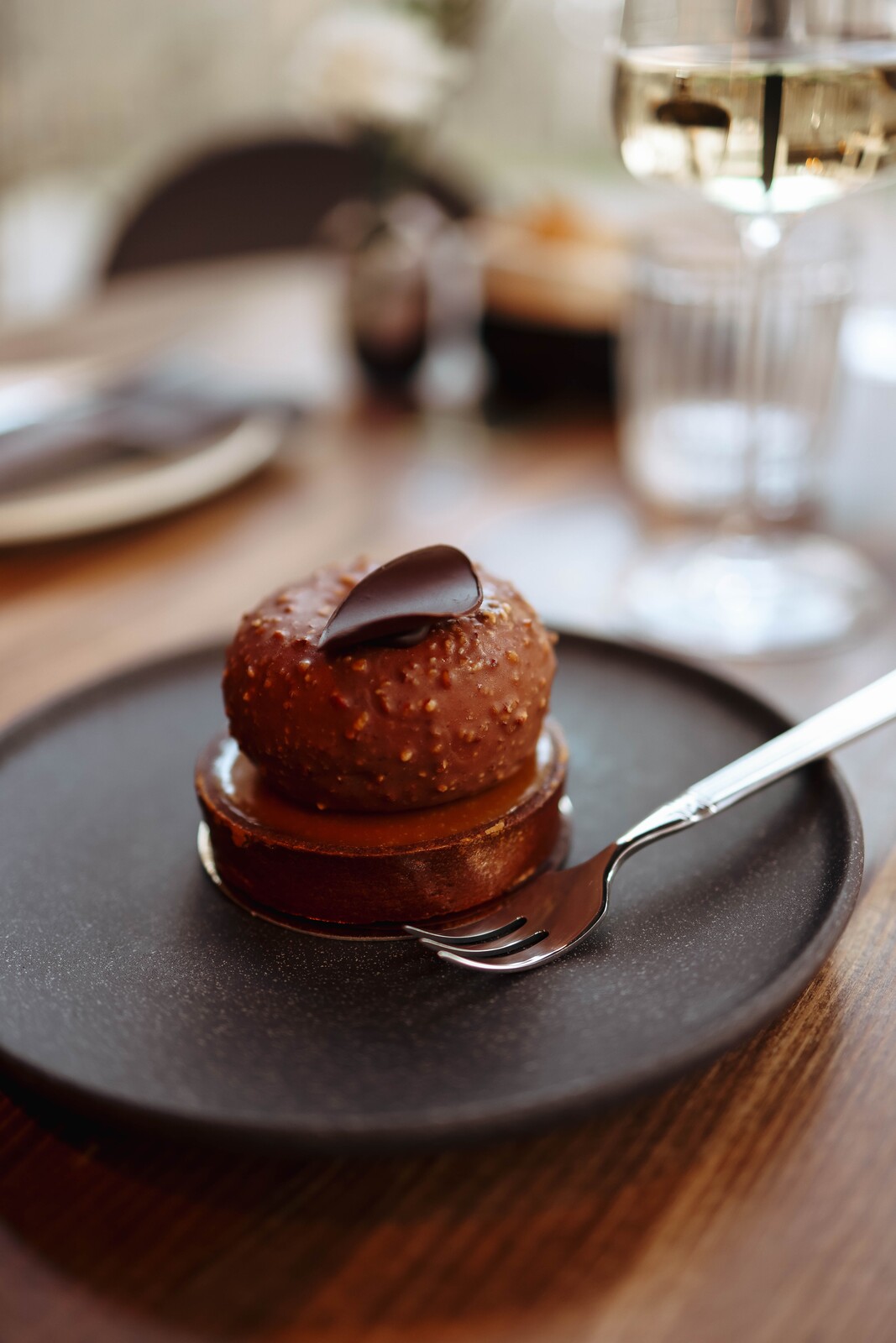 Chocolate dessert on a dark plate with a fork and soft glasses in the background