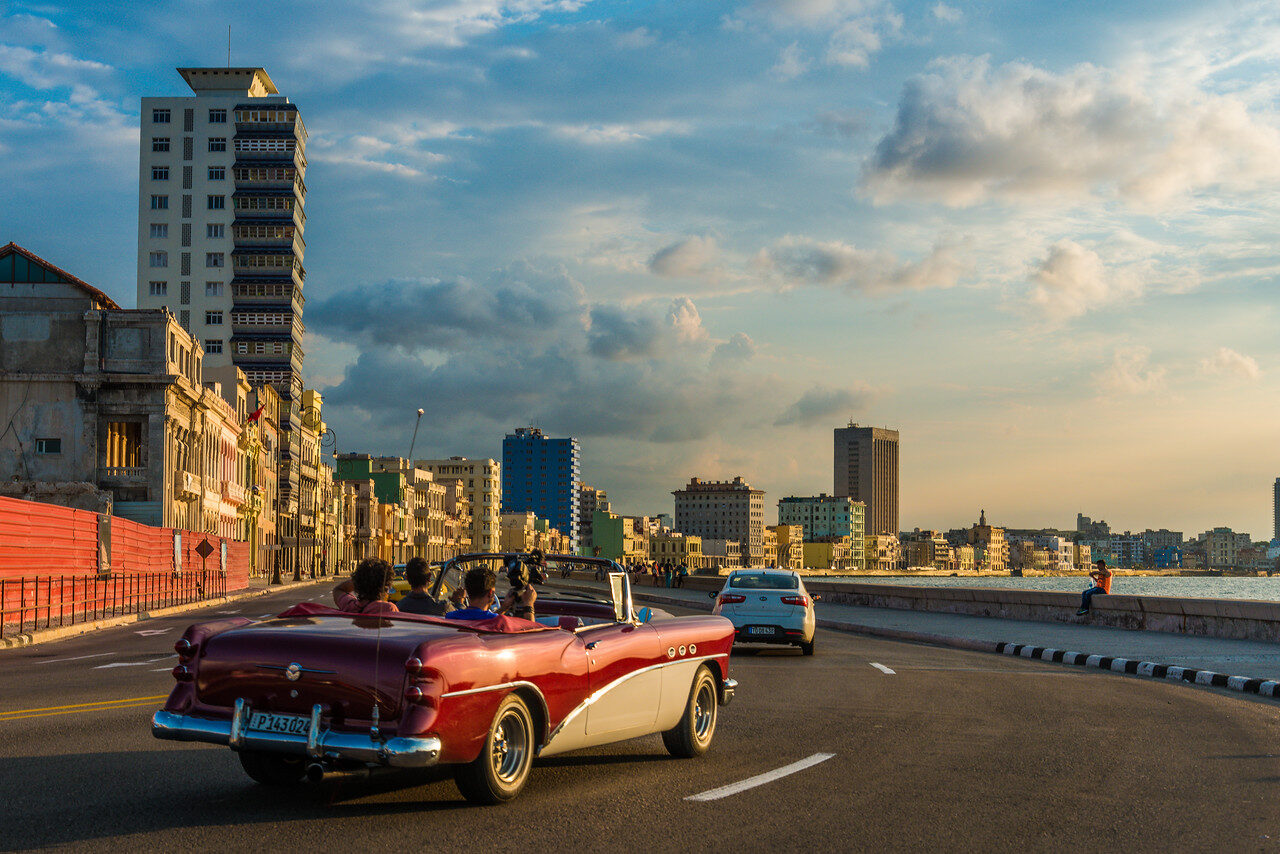 Pink vintage convertible on Havana's Malecón beside the sea and city buildings in warm evening light