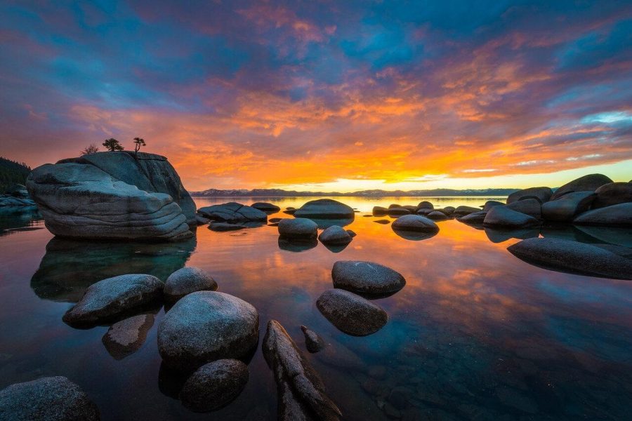 Orange sunset clouds reflected around Bonsai Rock at Lake Tahoe