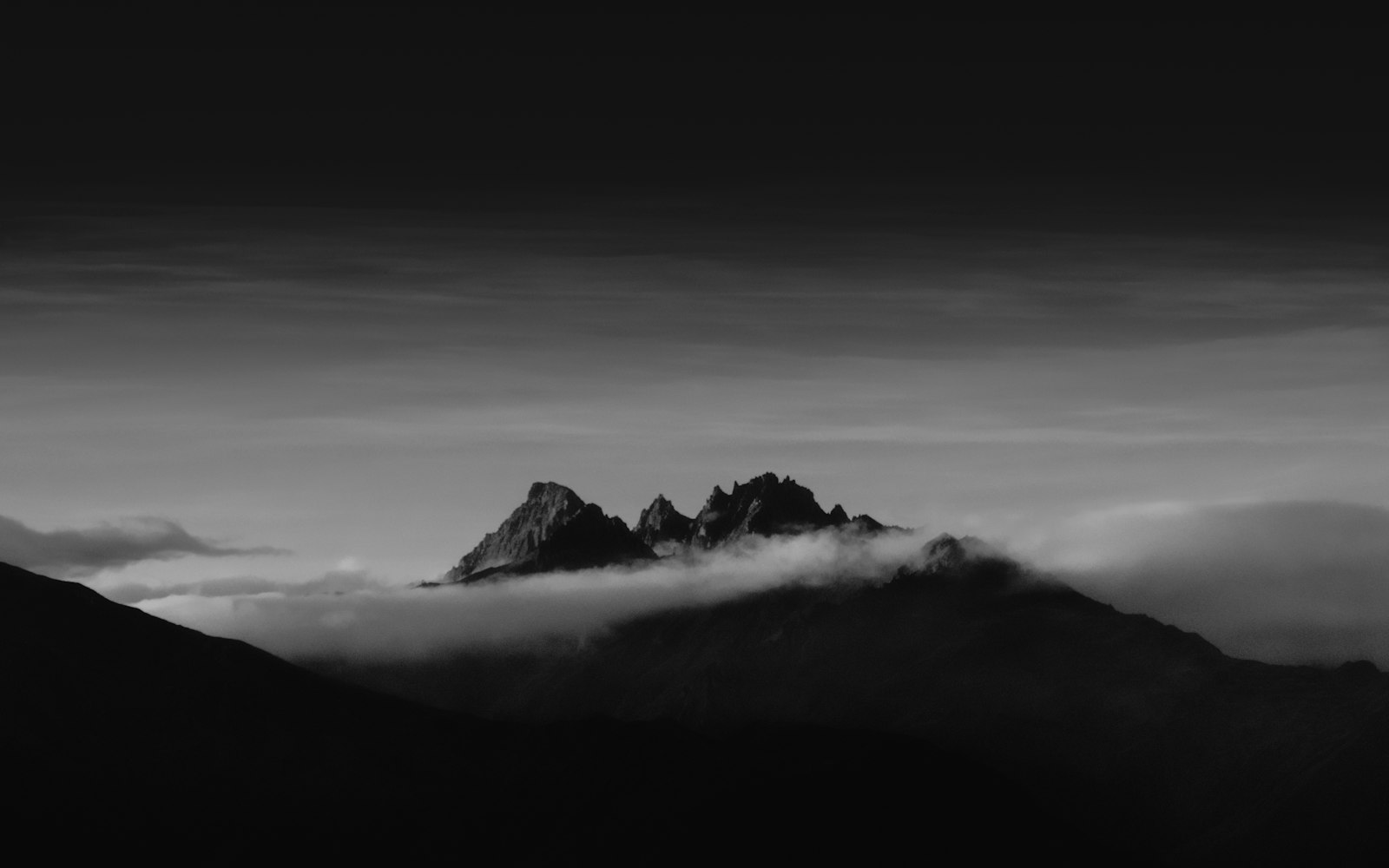 Grayscale photograph of the jagged Minaret Peaks breaking through a layer of clouds, New Zealand