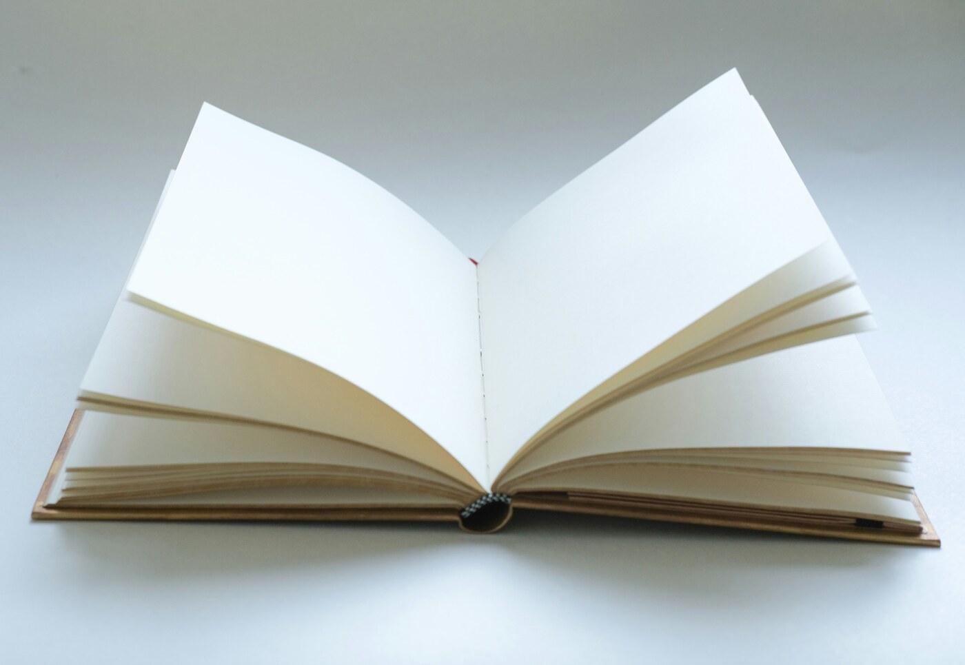An open hardcover book with blank cream pages fanned out and a visible spine on a pale surface