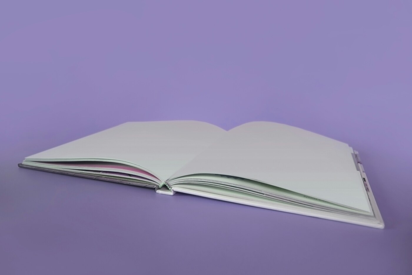 A blank open book with white pages lying on a purple background
