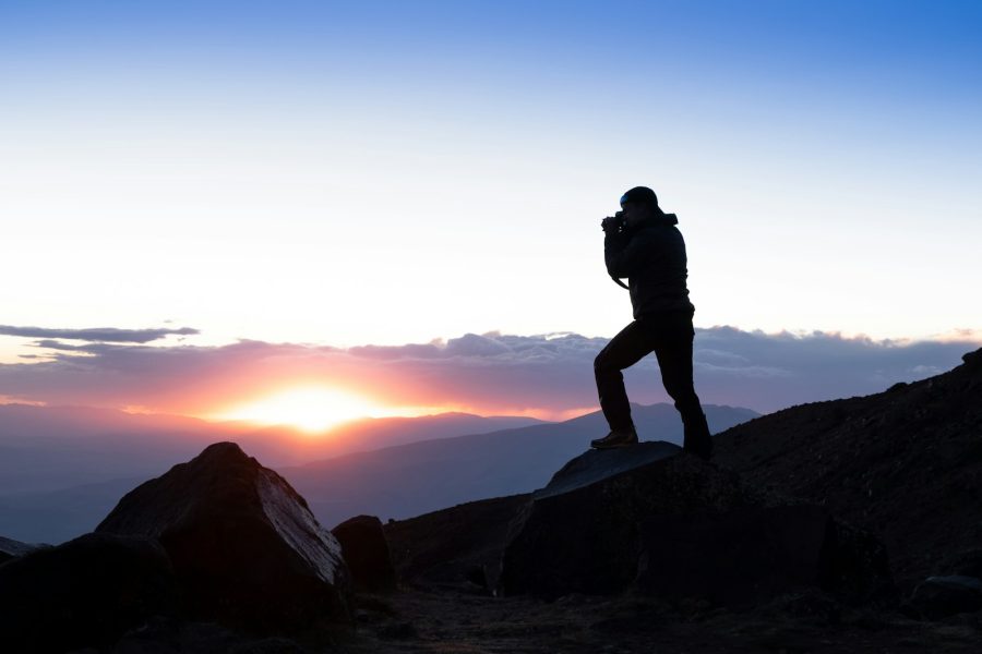 Photographer silhouetted on a rocky mountain at sunset above distant ridges