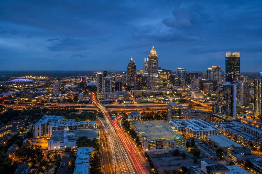 Atmospheric high-vantage view of Atlanta during blue hour, glowing city lights, subtle motion blur in traffic