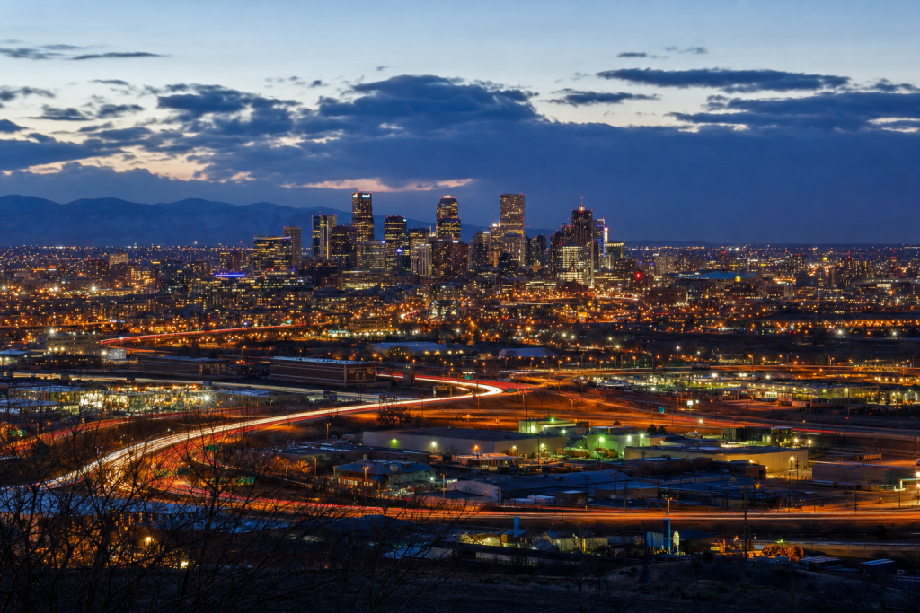 Atmospheric high-vantage view of Denver during blue hour, glowing city lights, subtle motion blur in traffic