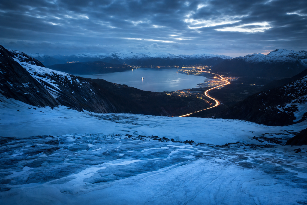 High-vantage view of Glacier during blue hour, glowing city lights, subtle motion blur in traffic