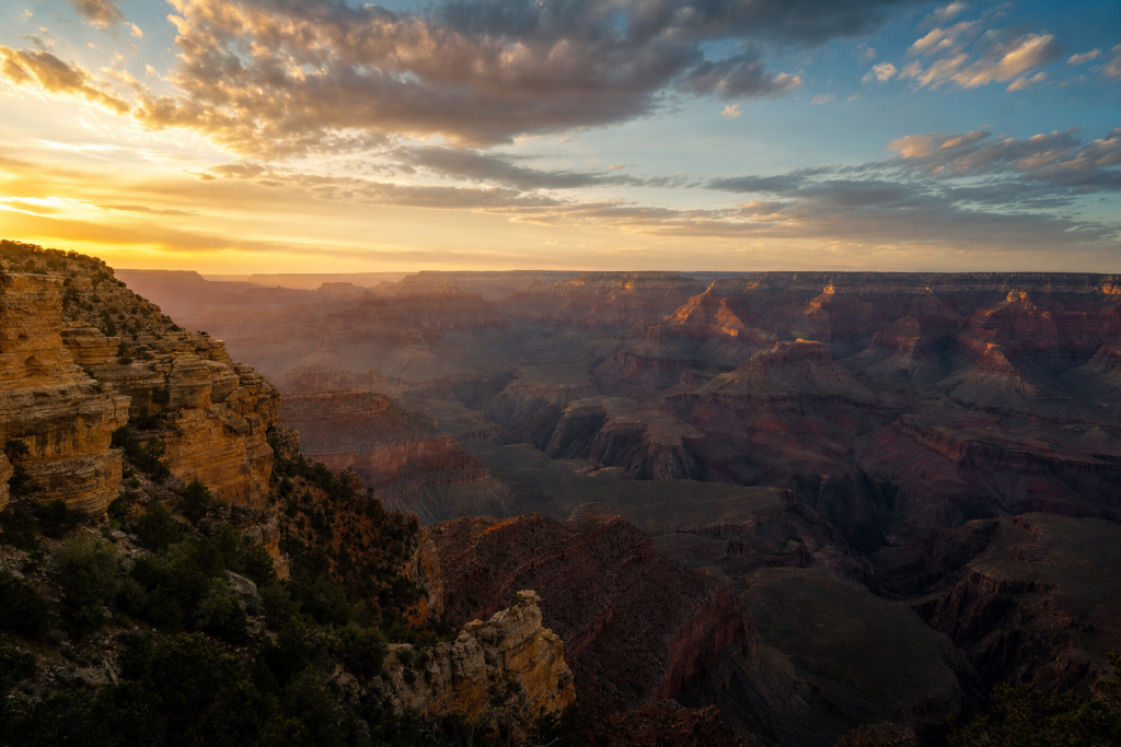 Wide-angle cinematic skyline of Grand Canyon at golden hour, iconic landmarks visible, dramatic warm light