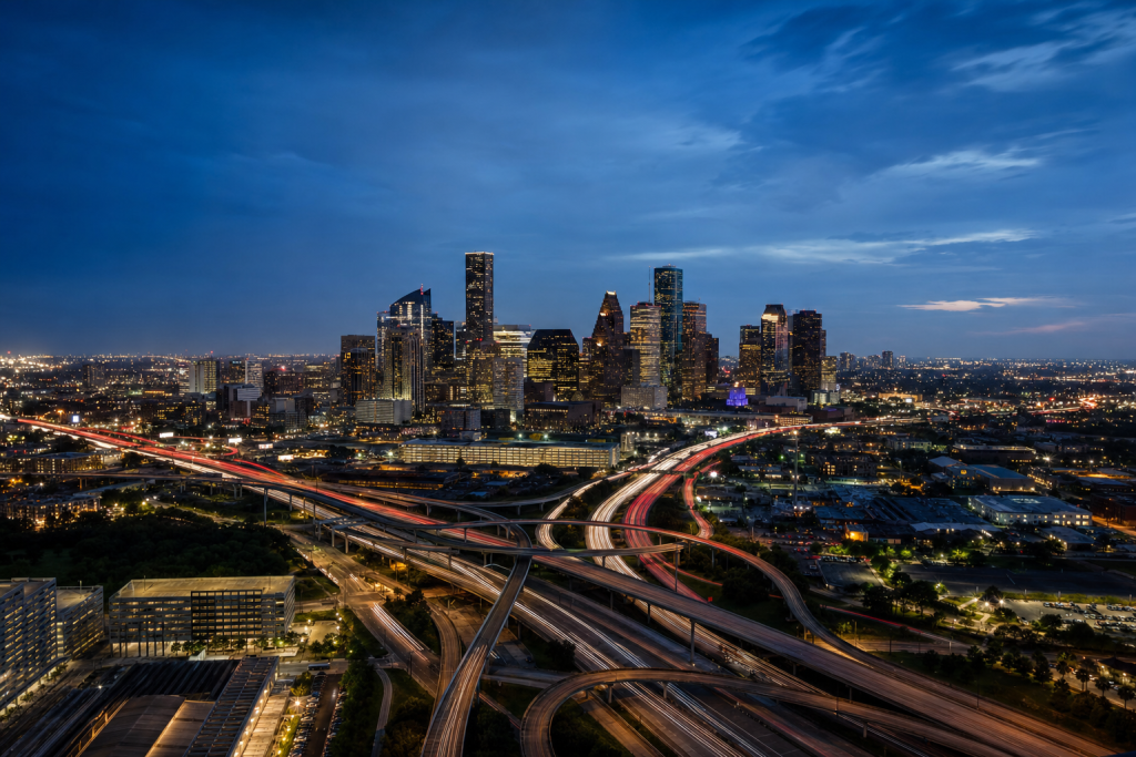 High-vantage view of Houston during blue hour, glowing city lights, subtle motion blur in traffic