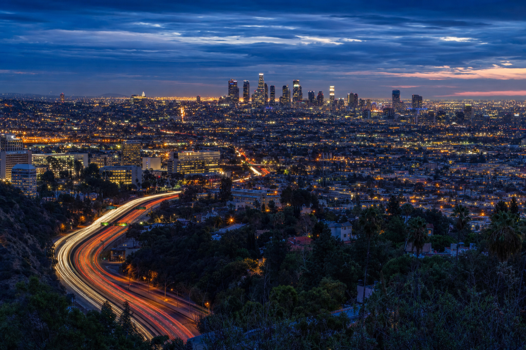 High-vantage view of Los Angeles during blue hour, glowing city lights, subtle motion blur in traffic