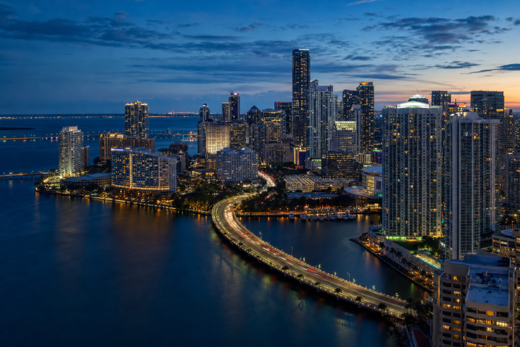 Atmospheric high-vantage view of Miami during blue hour, glowing city lights, subtle motion blur in traffic