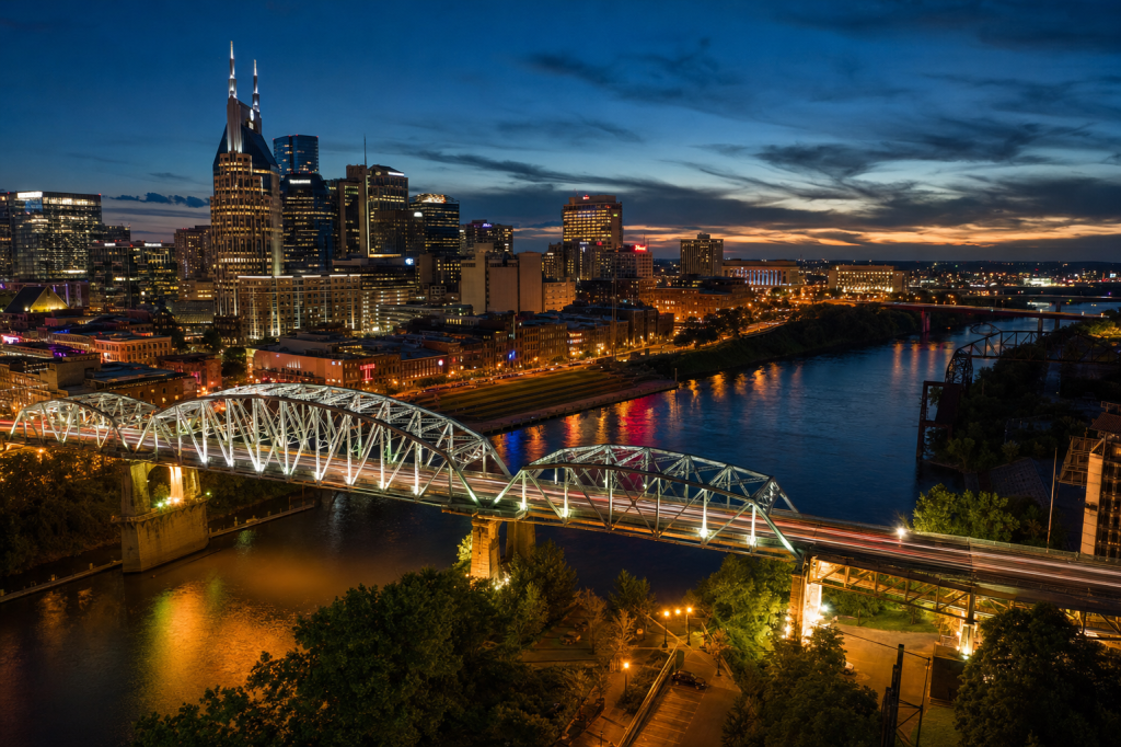 Atmospheric high-vantage view of Nashville during blue hour, glowing city lights, subtle motion blur in traffic