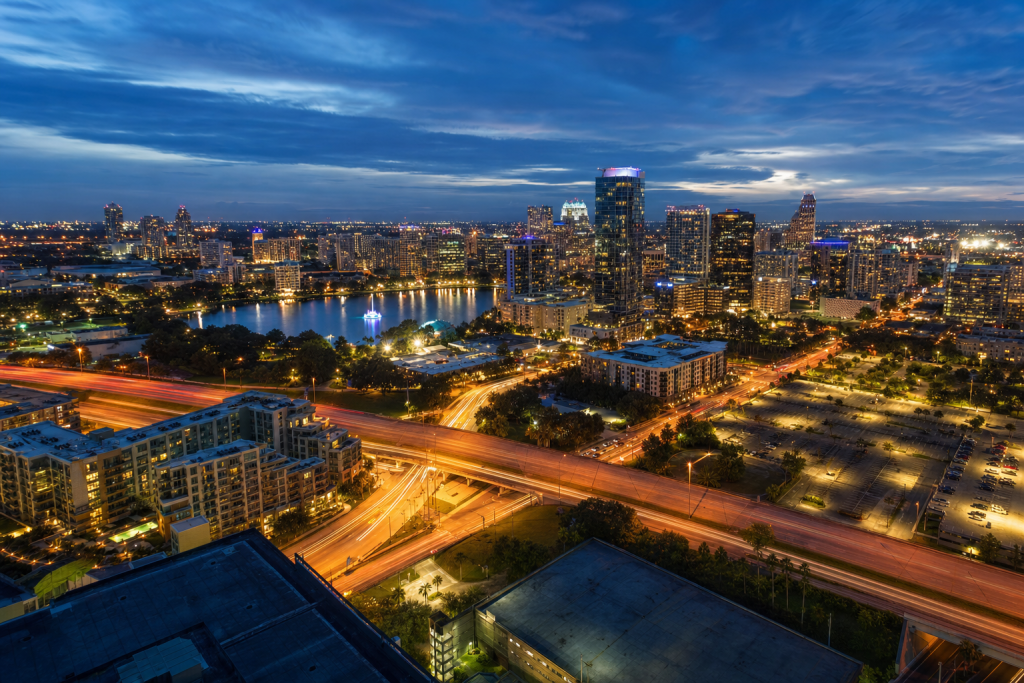 High-vantage view of Orlando during blue hour, glowing city lights, subtle motion blur in traffic