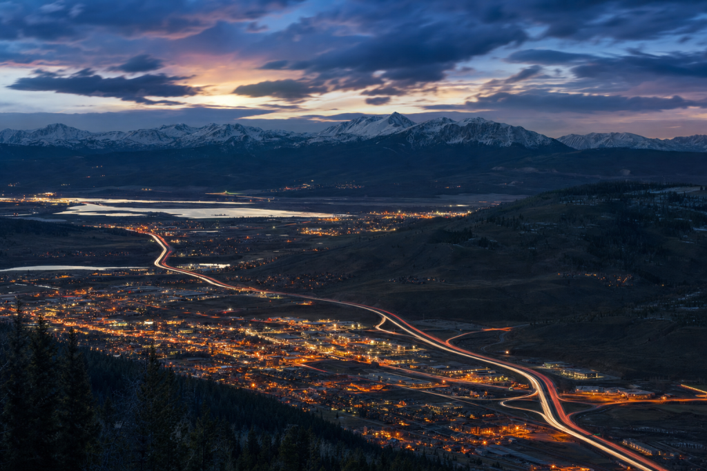 High-vantage view of Rocky Mountain during blue hour, glowing city lights, subtle motion blur in traffic