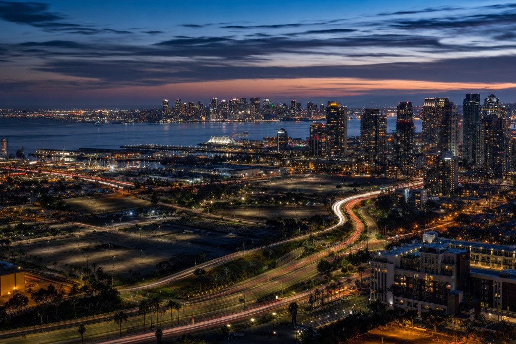 Atmospheric high-vantage view of San Diego during blue hour, glowing city lights, subtle motion blur in traffic