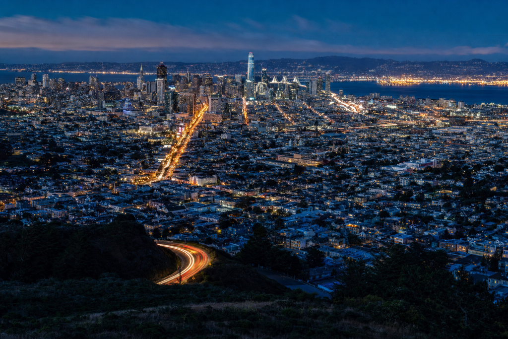 High-vantage view of San Francisco during blue hour, glowing city lights, subtle motion blur in traffic