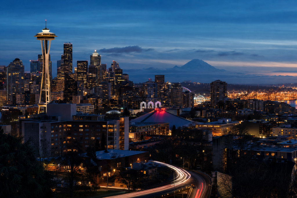 High-vantage view of Seattle during blue hour, glowing city lights, subtle motion blur in traffic